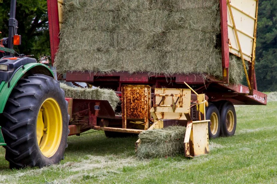 Tractor and hay baler working in a field with finished bales