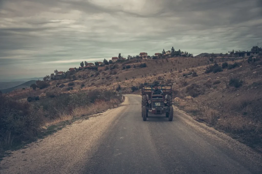 Tractor driving on a rural road through hills under a cloudy sky