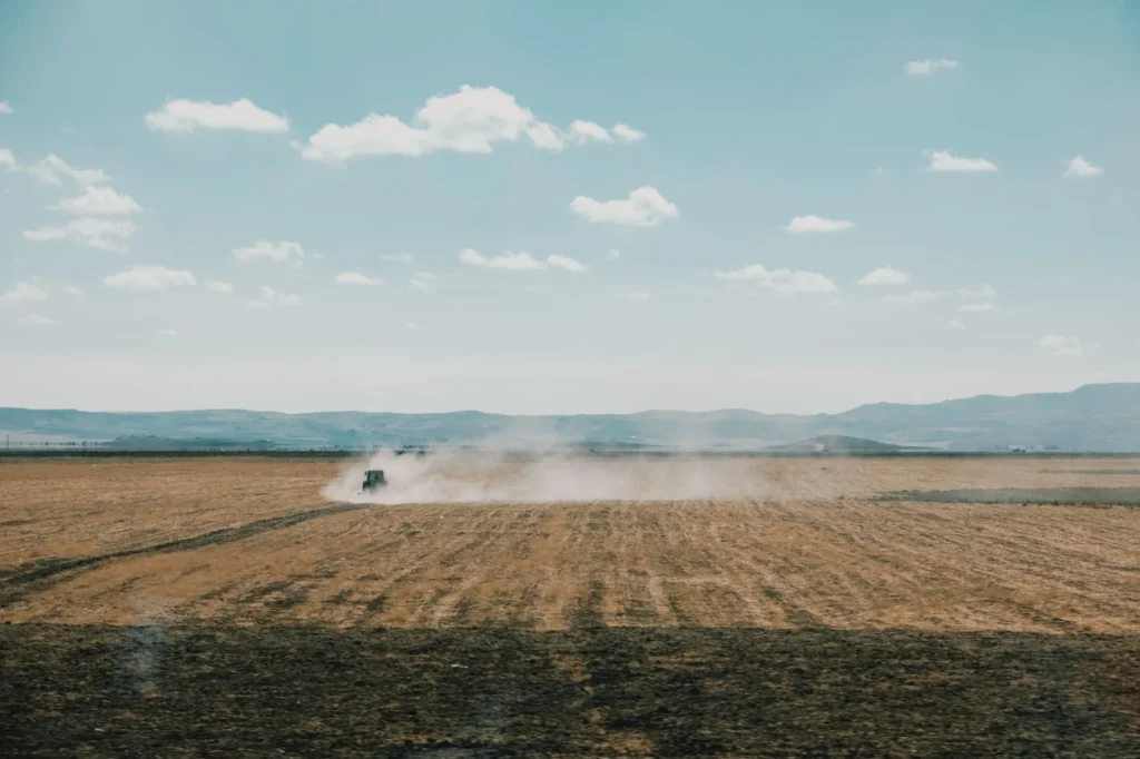 Trelleborg Tires: Who Owns Them, What They Make and Sizes We List A tractor creates dust as it works on a vast rural field under a clear sky, embodying the essence of agriculture.