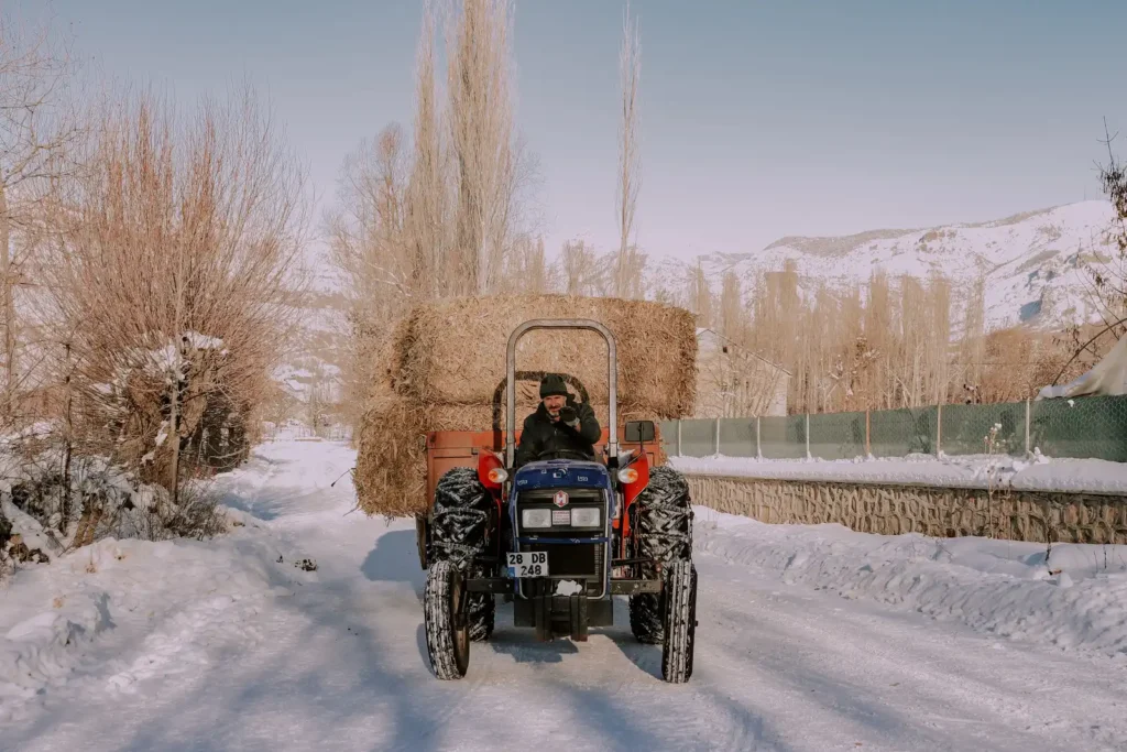Tractor carrying hay bales across a snowy farm