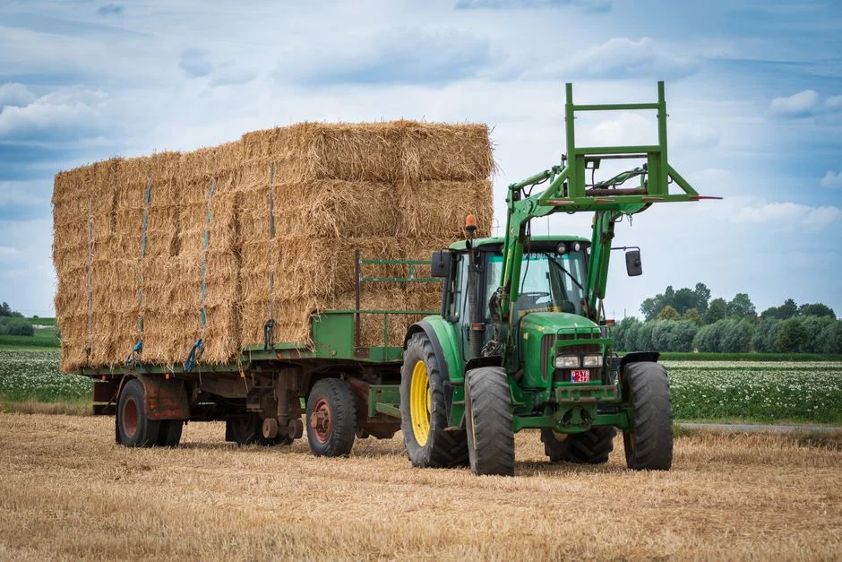 Tractor hauling a full trailer of hay bales across a field