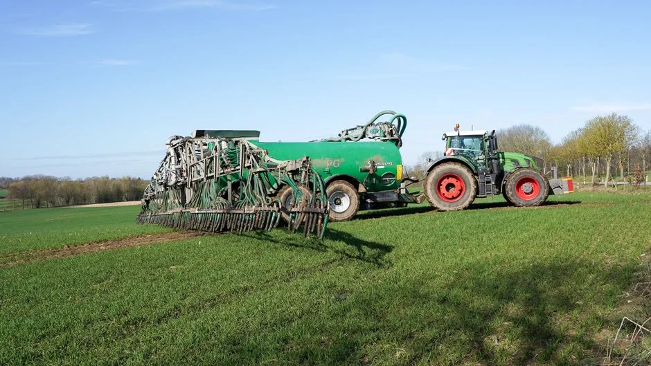 Tractor and manure spreader on green farmland in Lütau, Schleswig-Holstein, Germany.