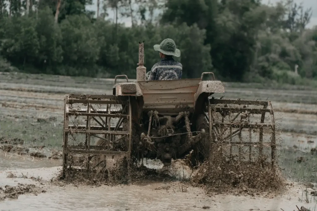 Firestone Tractor Tires: Who Makes Them and Which Line Fits Tractor plowing a muddy field where tread bar angle matters