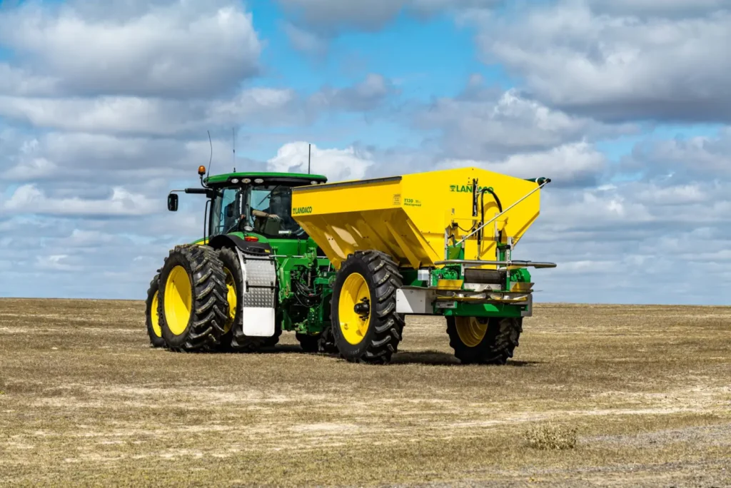 Modern tractor with a trailer sowing grain on a field under a cloudy blue sky