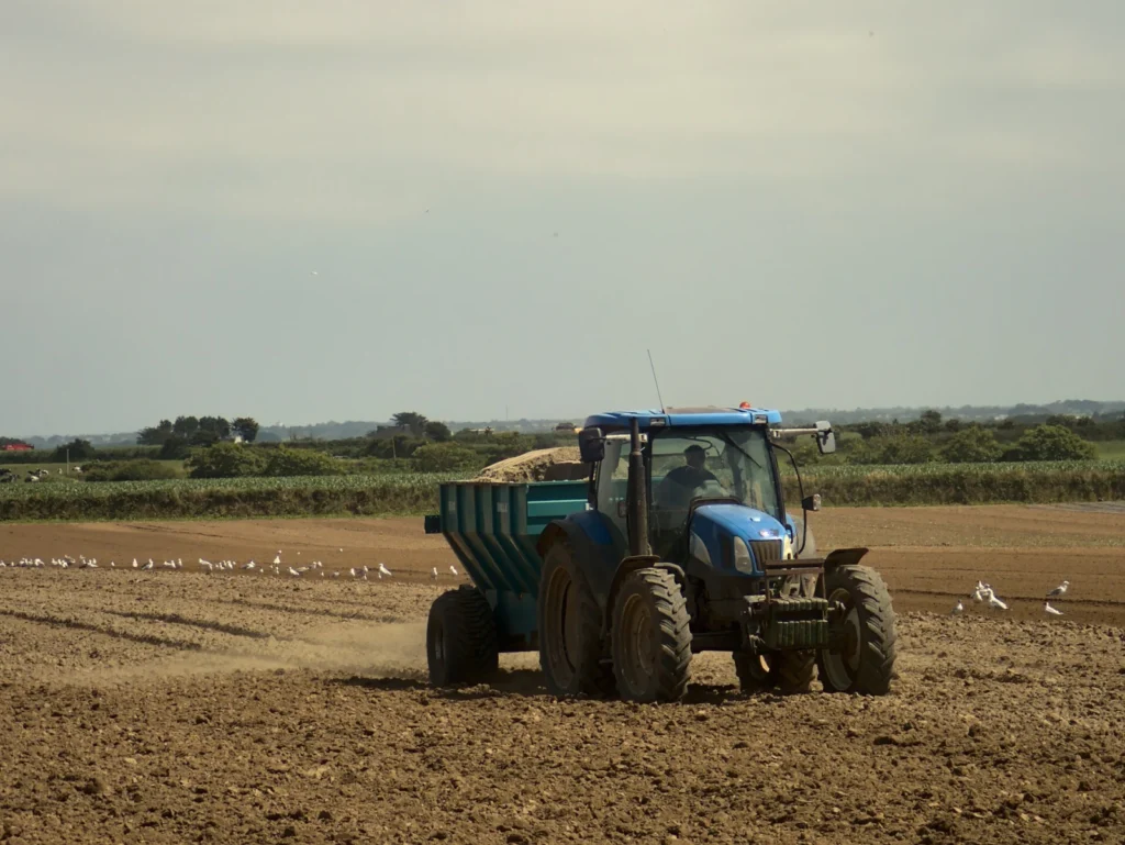 Blue tractor spreading fertilizer on a plowed field in Brittany
