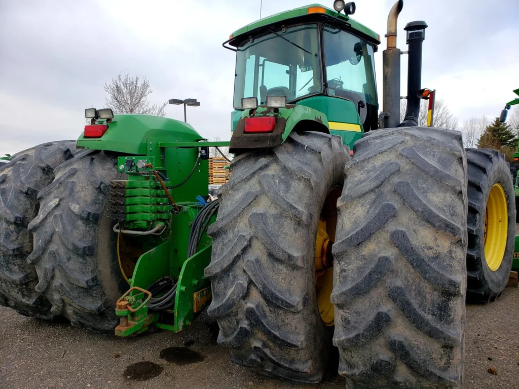 Large green tractor with big rear tires parked on a farm
