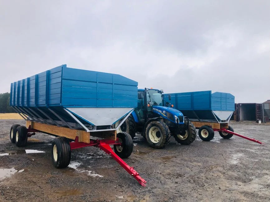Blue tractor towing grain wagons across a wet field