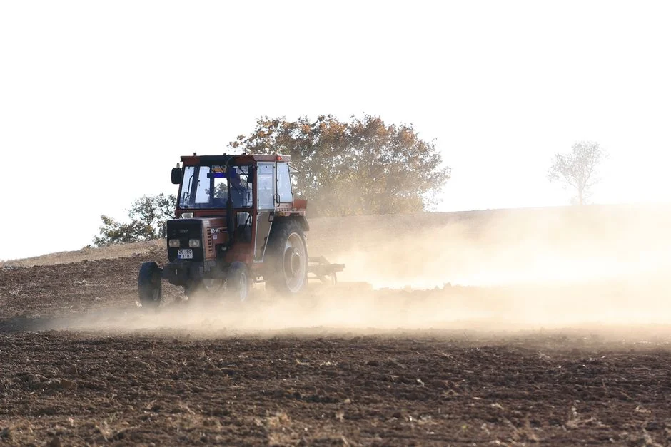 A farmer drives a red tractor through a dusty field, preparing for planting