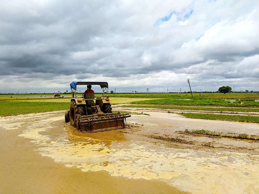 Tractor working on muddy farmland, showcasing rural agricultural scene with clouds overhead