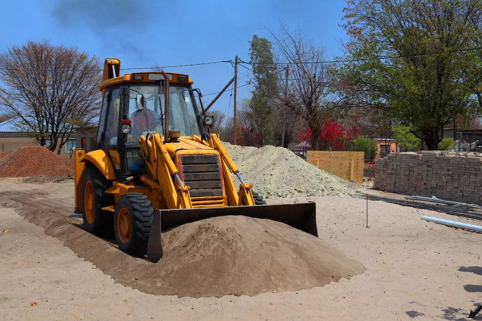 Yellow backhoe loader moving sand on a construction site