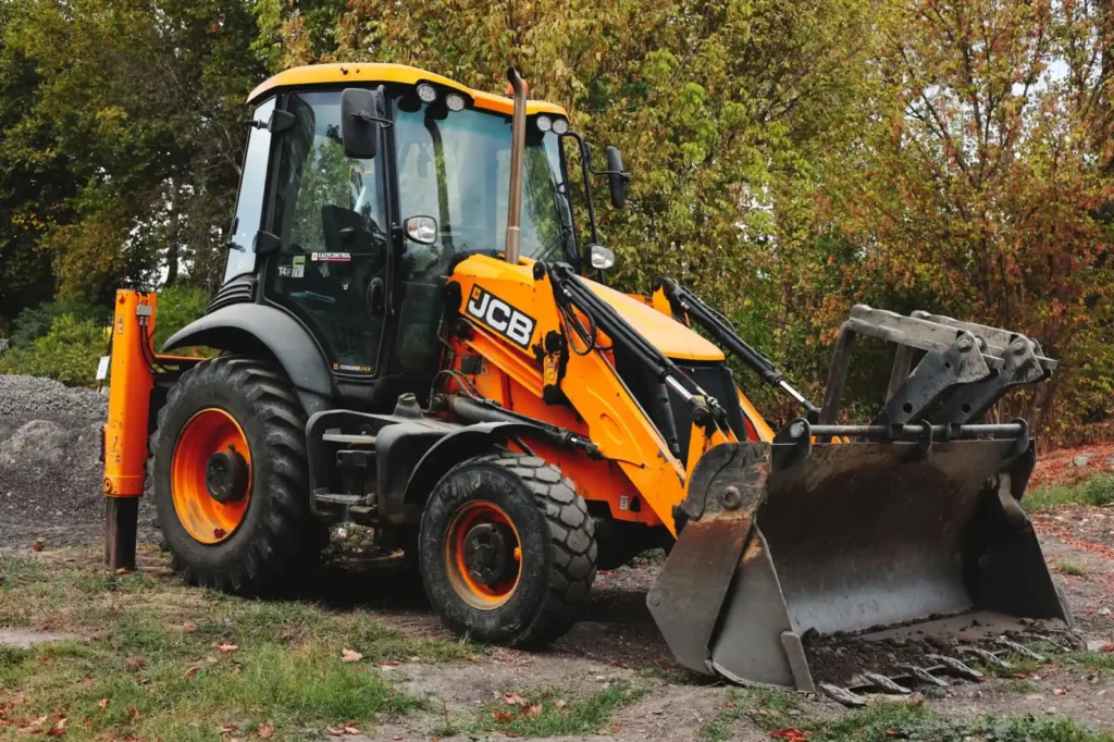 Yellow backhoe loader parked at a construction site among trees