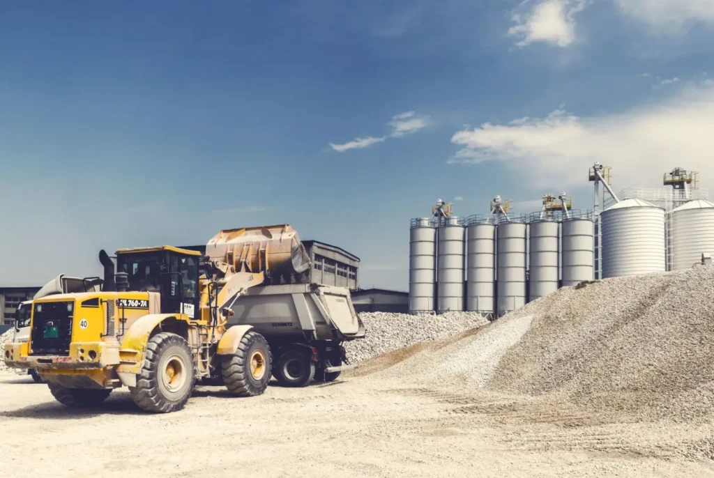 Yellow loader working in a gravel yard with silos behind it